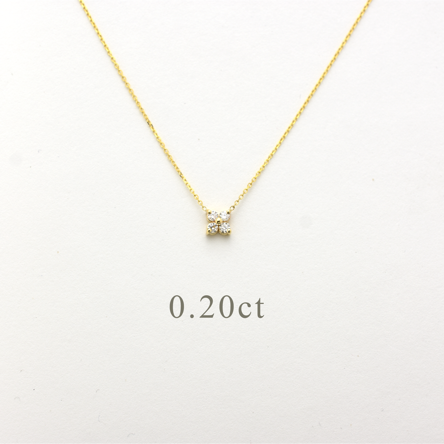 Close-up of a delicate 14K yellow gold chain necklace featuring a small, clover-shaped cluster pendant. The pendant consists of four brilliant round-cut diamonds totaling 0.20 carats, set closely together to create a tiny floral design. The necklace is displayed on a white background.