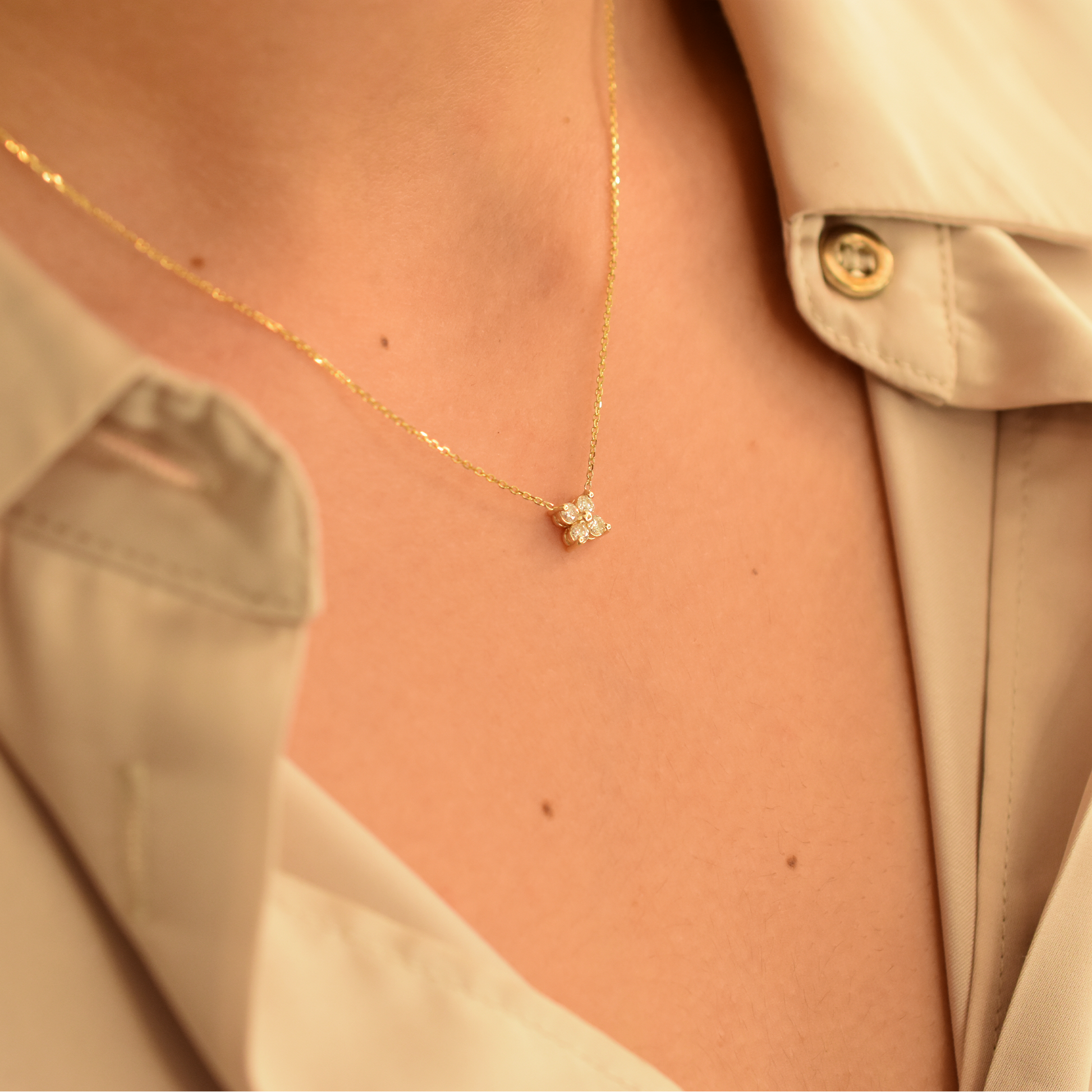 Gold necklace with a small cluster diamond pendant on a person wearing a beige shirt