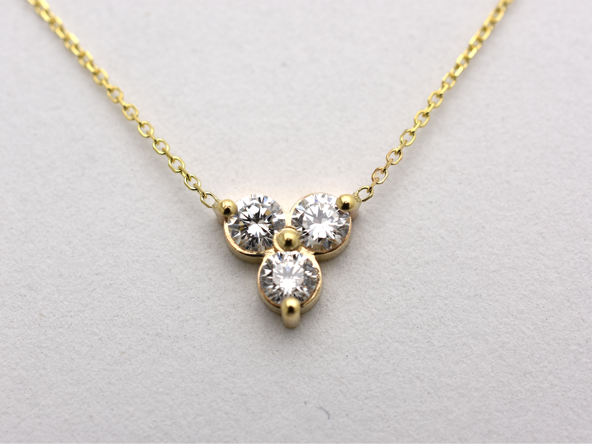 close up 14k yellow gold necklace with a three-stone pendant of round brilliant cut 0.60  carat diamonds  on a white background