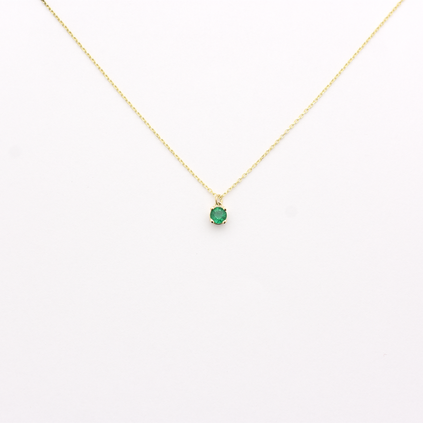A 14k gold necklace with a single emerald stone pendant. dangling