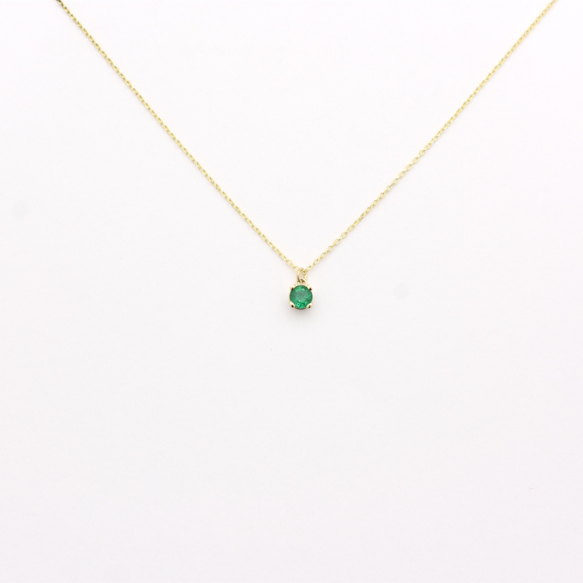 A 14k gold necklace with a single emerald stone pendant. dangling