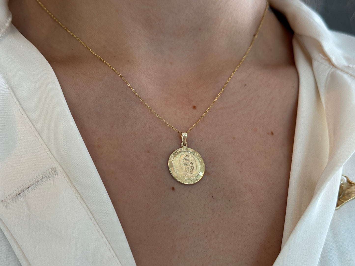 Gold guardian angel necklace with a Chain worn by a person in a white shirt.