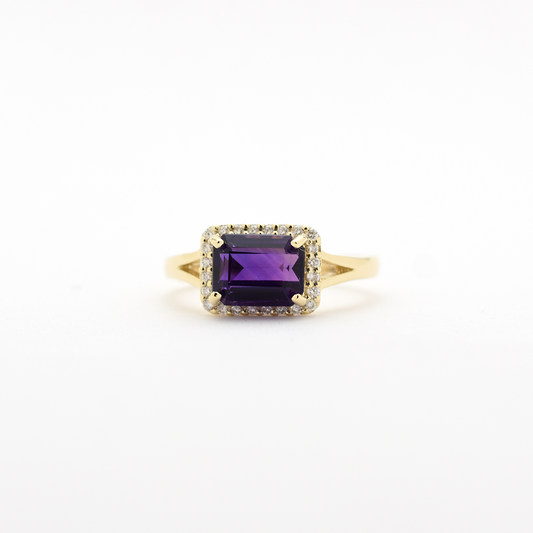 A 14k gold emerald cut amethyst diamond ring with smaller diamonds set around the main amethyst, on a white background.